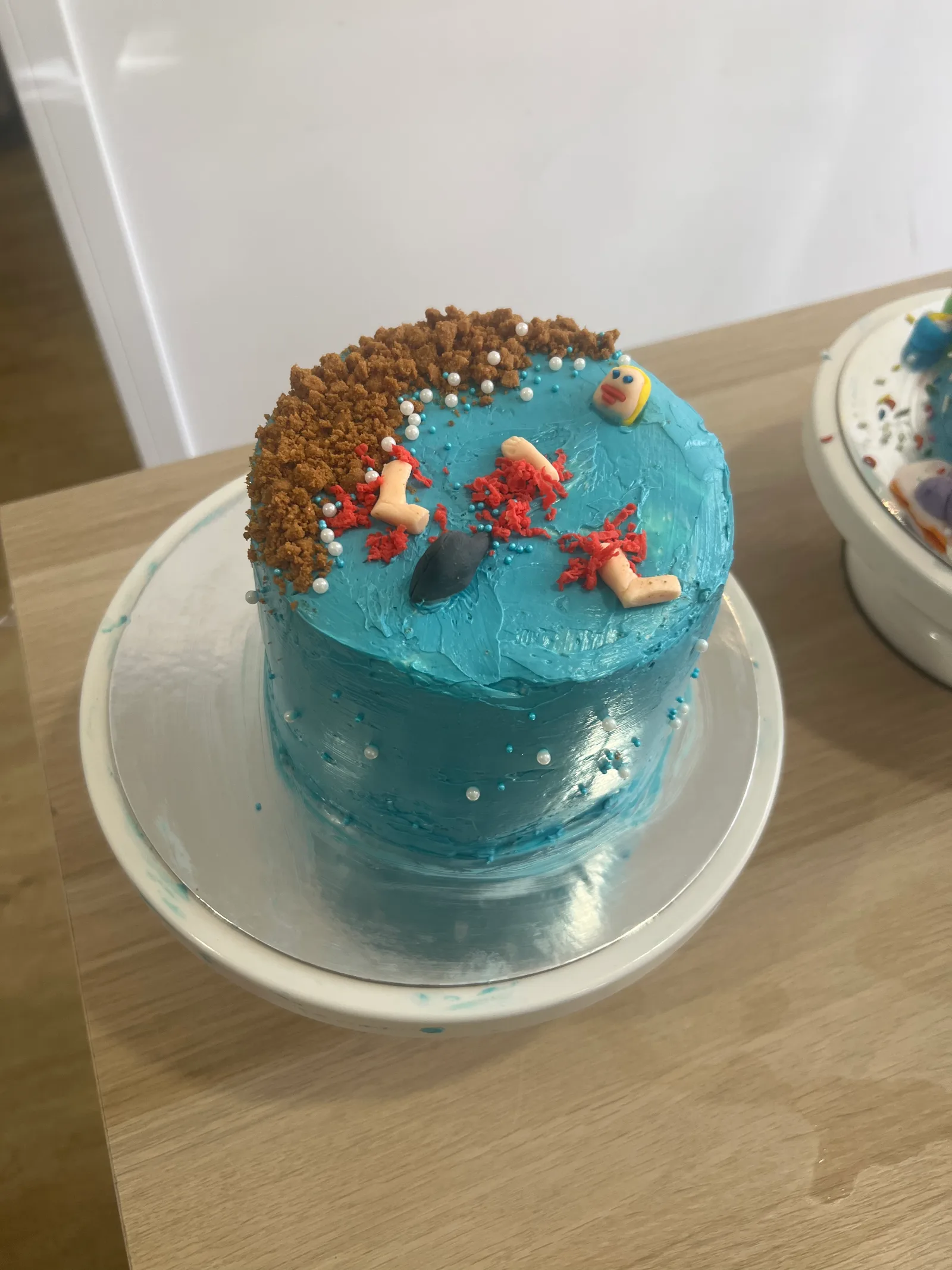 A Jaws cake: buttercream sea, biscuit-crumb beach, a shark fin and an unlucky fondant swimmer.