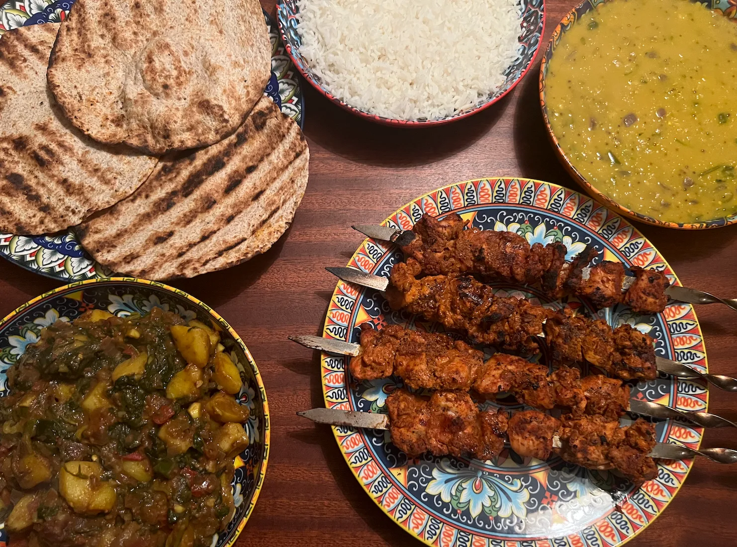 The full spread: tandoori kebabs, saag aloo, daal, rice and griddled rotis on patterned plates.